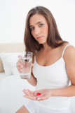 Woman looking worried as she is about to take two pills with water,
