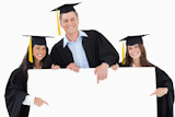Three graduates pointing to the blank sign as they look at the camera