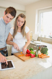 Woman cutting vegetables with man reading the cookery book