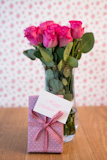 Bouquet,of,pink,roses,in,vase,with,pink,gift,leaning,against,it