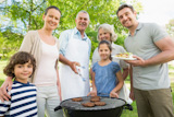 Extended family stands by using a barbecue in a park.