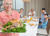 Grandmother,holding,chicken,roast,with,family,at,dining,table