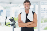 Smiling man standing with arms crossed at spinning class in bright gym