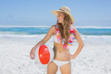 Fit smiling blonde in white bikini and straw hat holding beach ball