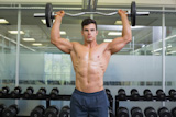 Shirtless muscular man lifting barbell in gym