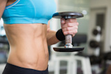 Mid section of fit woman exercising with dumbbell in gym